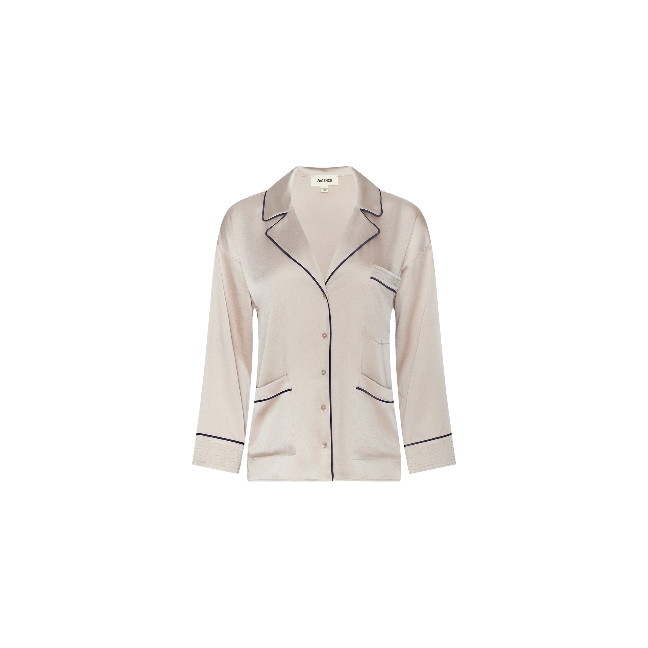 The Mara Blouse is a light pink satin pajama top featuring black piping, long sleeves, a notched collar, button front closure, and a single chest pocket. Displayed on a plain white background, this relaxed-fit blouse offers elevated comfort ideal for loungewear.