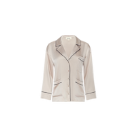 The Mara Blouse is a light pink satin pajama top featuring black piping, long sleeves, a notched collar, button front closure, and a single chest pocket. Displayed on a plain white background, this relaxed-fit blouse offers elevated comfort ideal for loungewear.