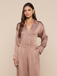 A woman models the Mara Blouse, a silky light brown satin top paired with matching relaxed-fit pants. She stands with one hand in her pocket against a plain light background—a perfect look for stylish loungewear.
