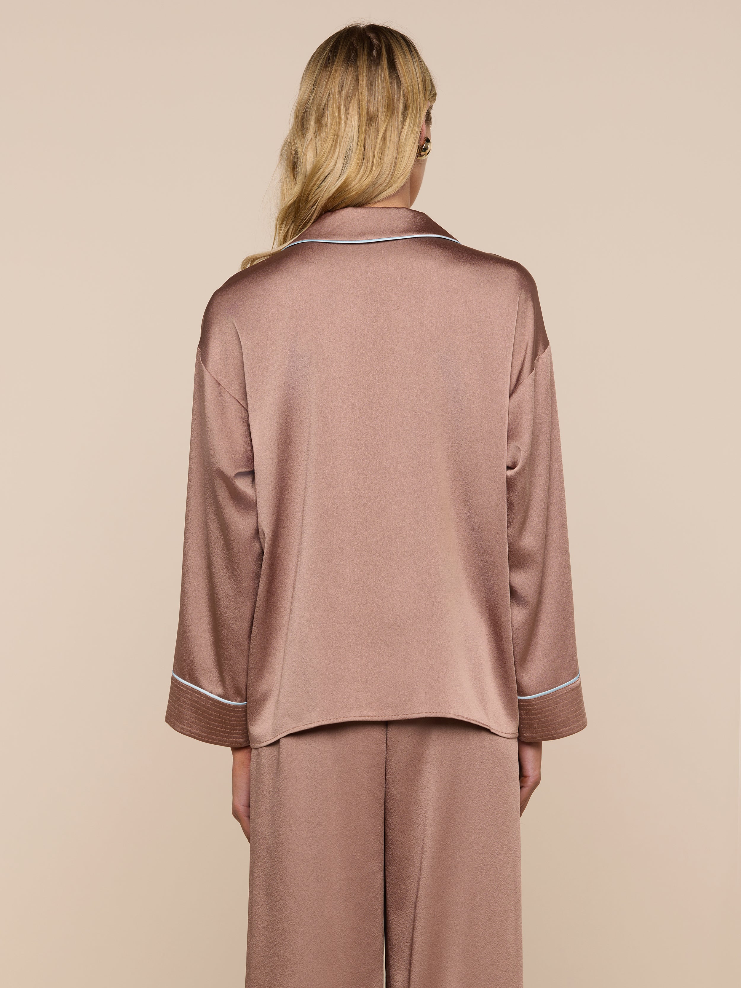A person with long blonde hair is seen from behind, wearing a relaxed fit, silky brown Mara Blouse and matching bottoms as a loungewear set, standing against a plain light background.