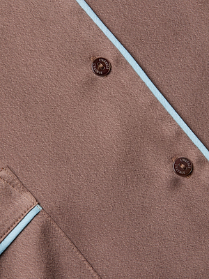 Close-up of the Mara Blouse brown loungewear fabric featuring two brown LANVIN PARIS buttons, light blue piping on the seams, and a partial pocket in the lower left corner.