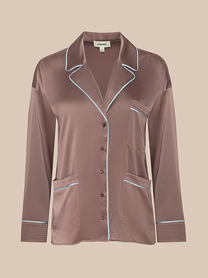The Mara Blouse is a silky brown button-up pajama top with long sleeves, three front pockets, and light blue piping on the collar, cuffs, pockets, and front edges, shown against a plain beige background.