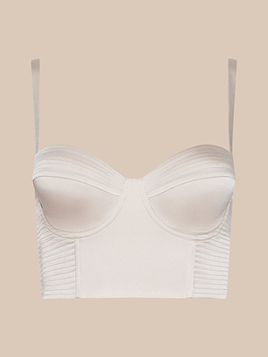 The Nysa Bustier Top is a light beige, structured bustier with underwire and molded cups, thin adjustable straps, and ribbed detailing along the sides and top edge, shown against a plain beige background.
