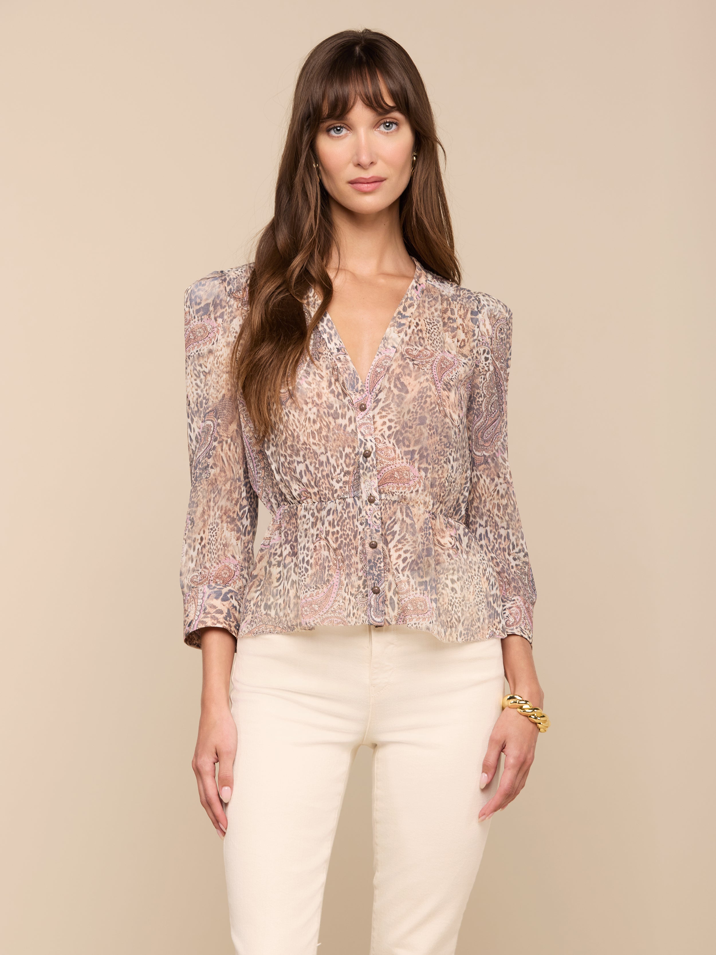 A woman with long brown hair wears the Suri Top—a sheer poly chiffon blouse featuring puff sleeves and a paisley animal print—paired with light-colored pants, standing against a plain light background.