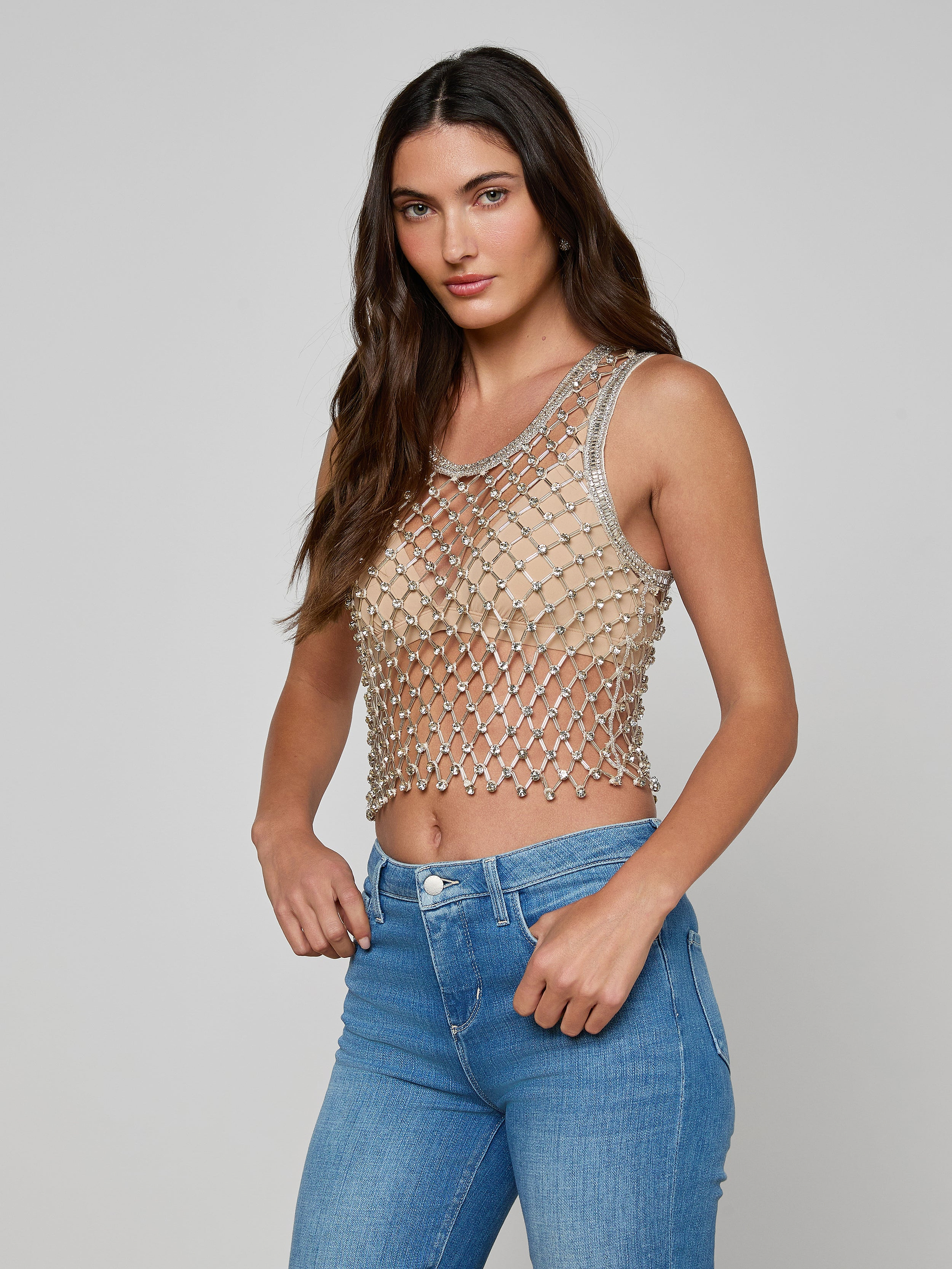A woman wearing the Freia Crystal Tank over a nude bralette and blue jeans stands against a plain, light background.