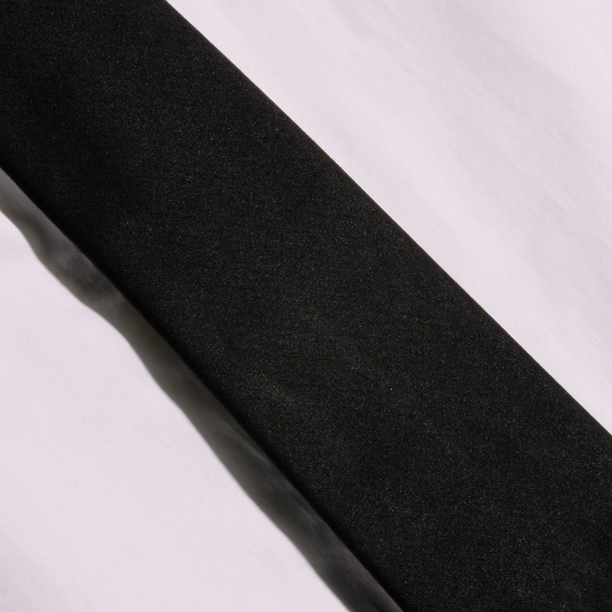 A Wren Neck-Tie Top, in black and featuring a sleek rectangular silhouette, is displayed diagonally across a white, slightly wrinkled surface, with contrasting light and shadows evoking the modern lines of New York Fashion Week.