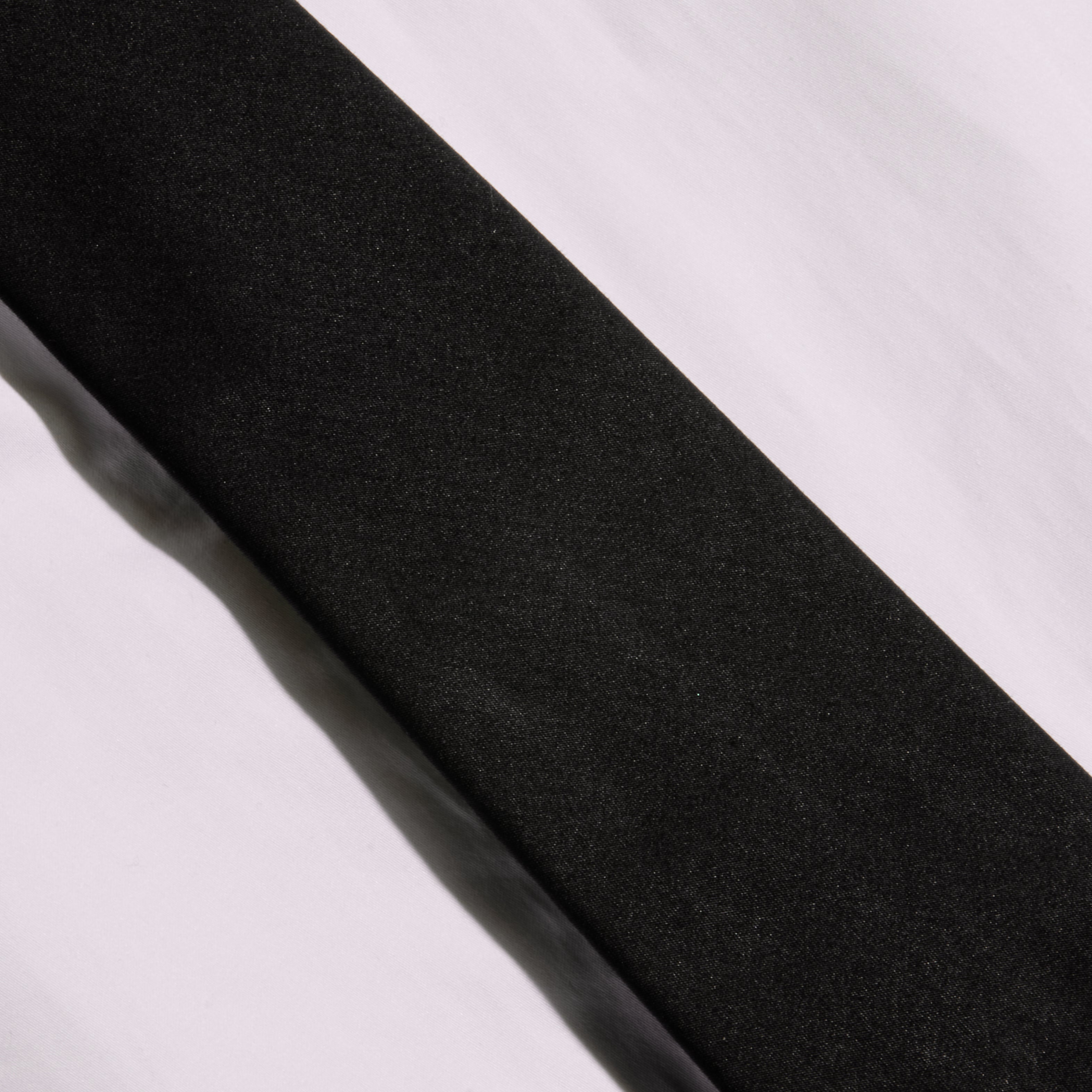A Wren Neck-Tie Top, in black and featuring a sleek rectangular silhouette, is displayed diagonally across a white, slightly wrinkled surface, with contrasting light and shadows evoking the modern lines of New York Fashion Week.