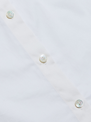 Close-up of the Wren Top, a white sateen cotton shirt featuring four pearly white buttons sewn in a diagonal row on smooth fabric, highlighting its fine texture and stitching details.
