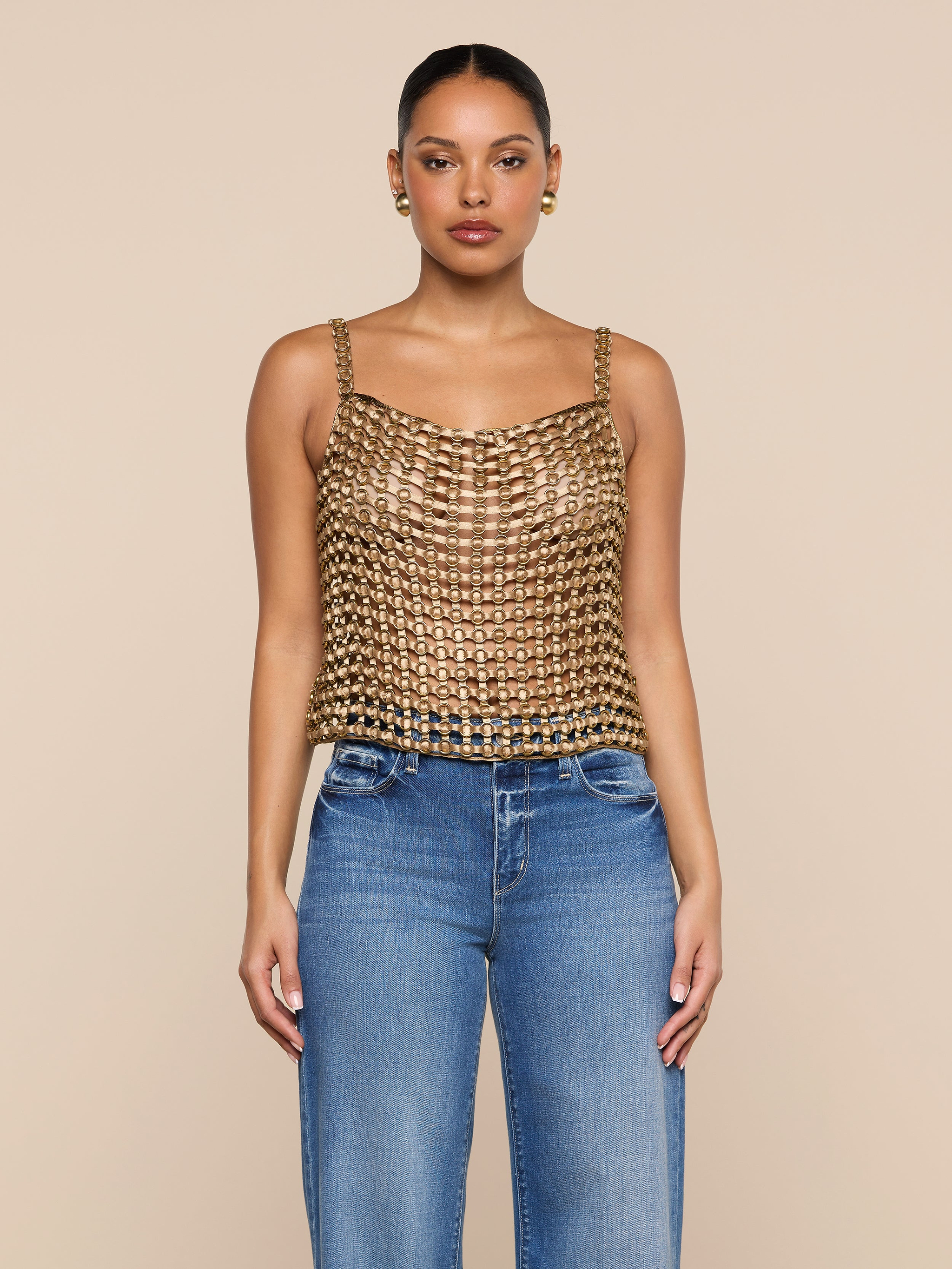A woman stands facing forward, wearing the Joanette Embellished Tank with a gold chainmail-style design and blue jeans against a plain white background.