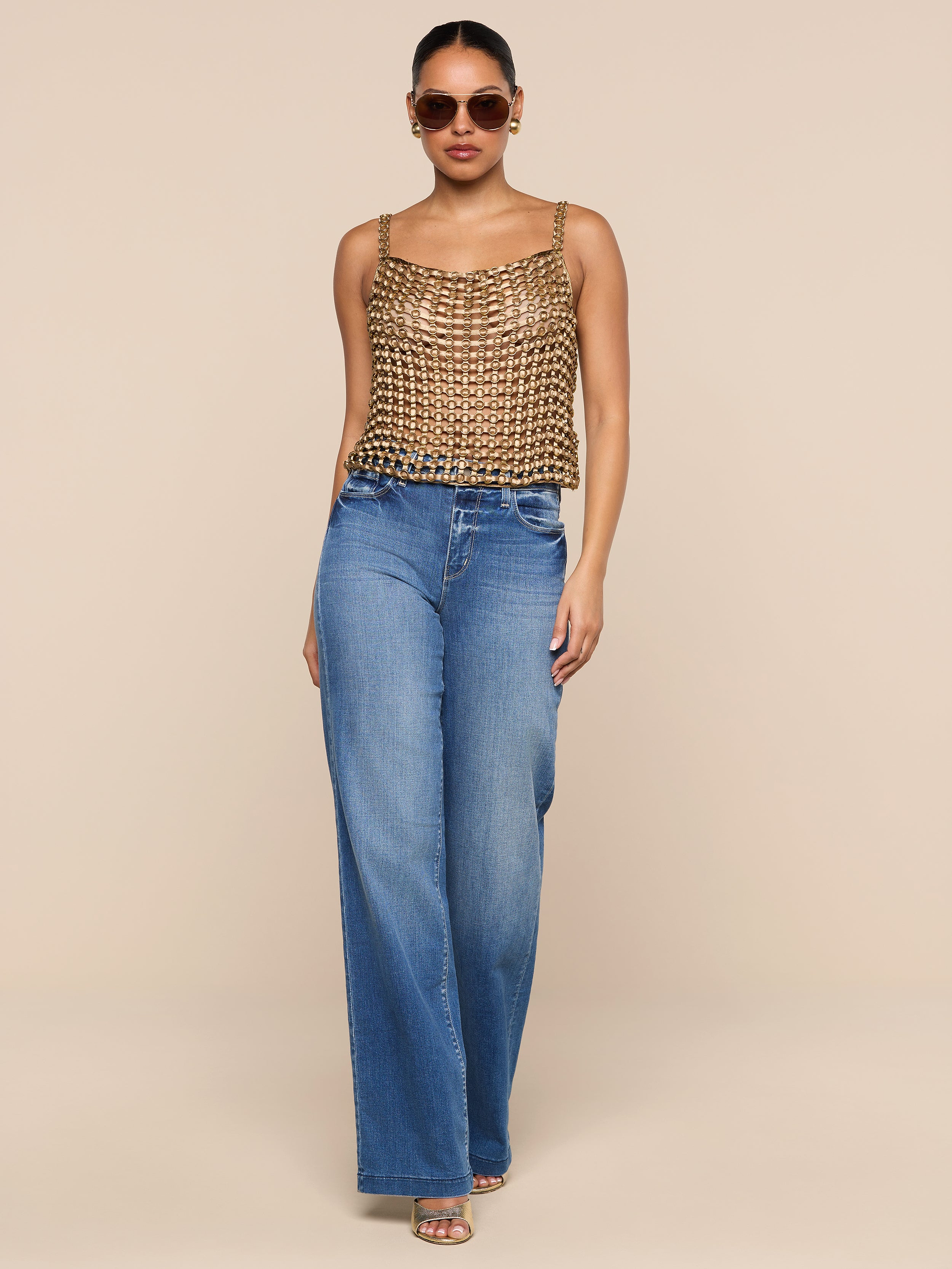 A woman wearing sunglasses, the Joanette Embellished Tank, wide-leg blue jeans, and heels stands against a plain white background.