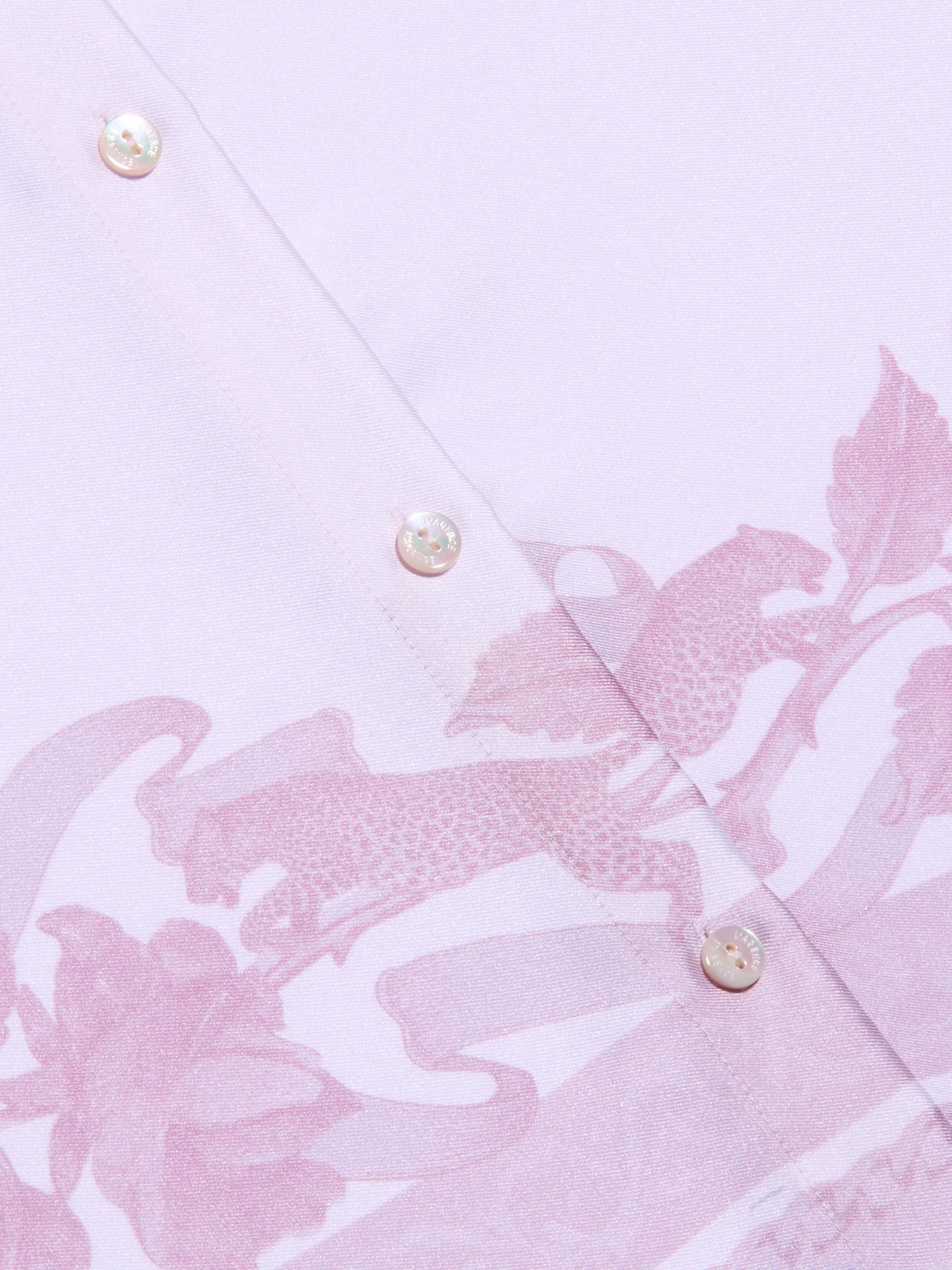 Close-up of the Judy Blouse, a light pink button-down shirt featuring two white buttons and a subtle leopard print and floral pattern in a slightly darker pink shade.