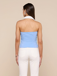 A woman stands with her back to the camera, wearing the light blue Rina Poplin Halter Top and white pants against an off-white background.
