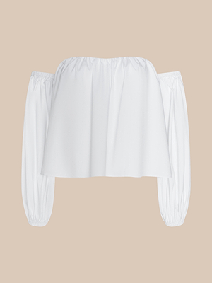 The Sarai Off-the-Shoulder Top, made from organic cotton, features long loose gathered sleeves with an elastic neckline and cuffs. Shown in white against a beige background.