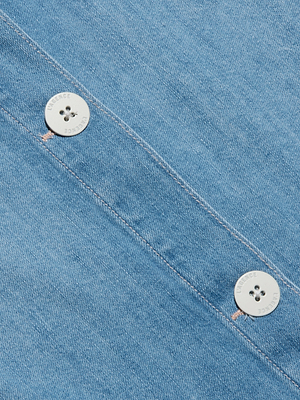 Close-up of blue denim fabric with two white buttons sewn along a diagonal seam. The buttons have four holes and subtle engraved text around their edges. The texture of the denim is clearly visible.