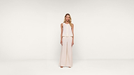 A woman stands facing forward, wearing a sleeveless, light beige top and matching wide-leg pants against a plain white background.