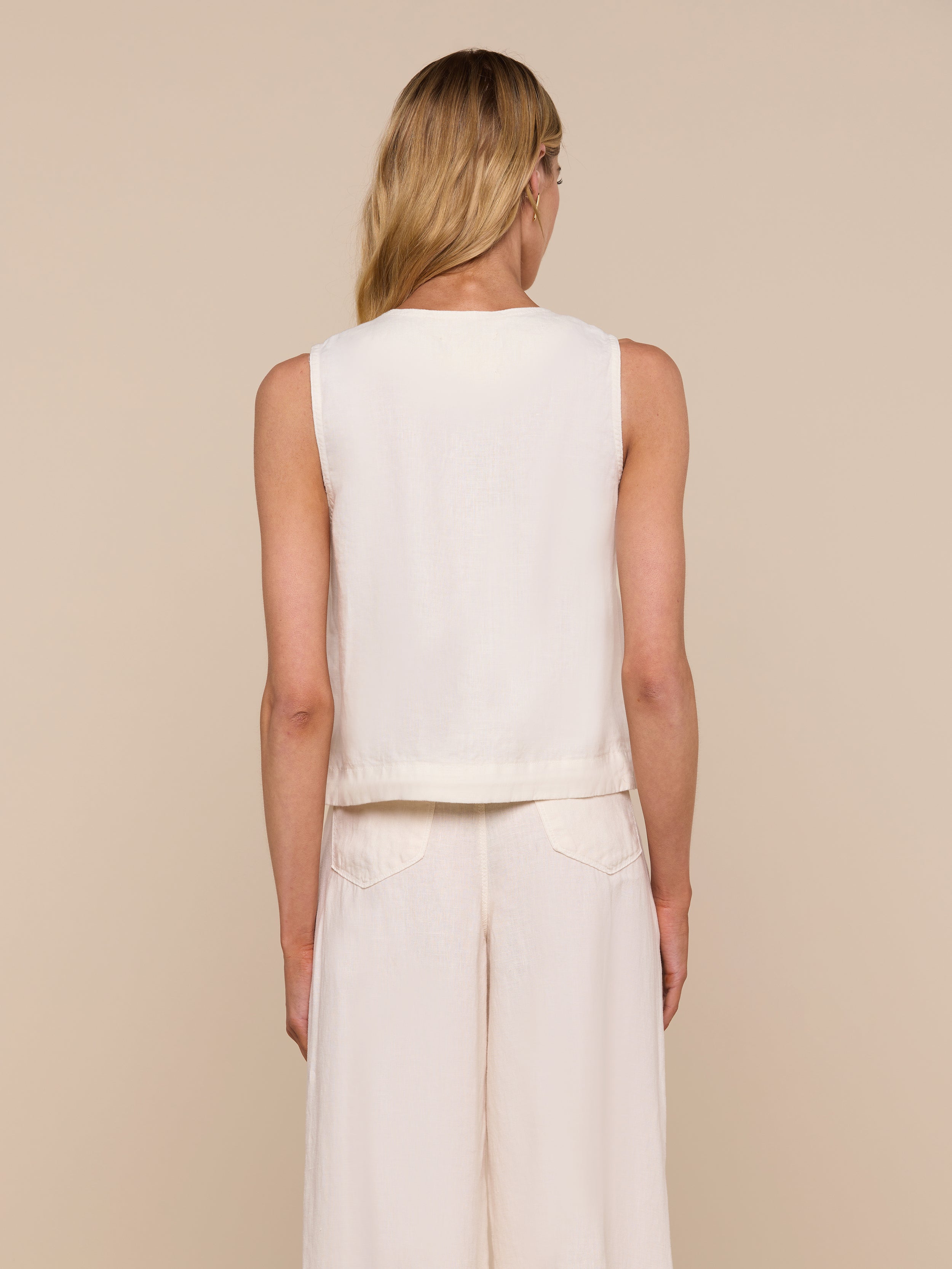 A woman with long blonde hair is shown from the back, wearing the sleeveless Foster Linen Top and matching wide-leg pants with an A-line silhouette against a plain light background.