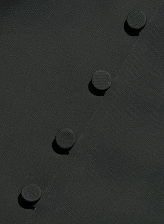 Close-up of five black fabric-covered buttons arranged diagonally on a matching black Zinnia One-Shoulder Top, possibly part of its sculptural silhouette. The textured buttons and smooth fabric create a subtle contrast, highlighting the refined details characteristic of this tailored design.