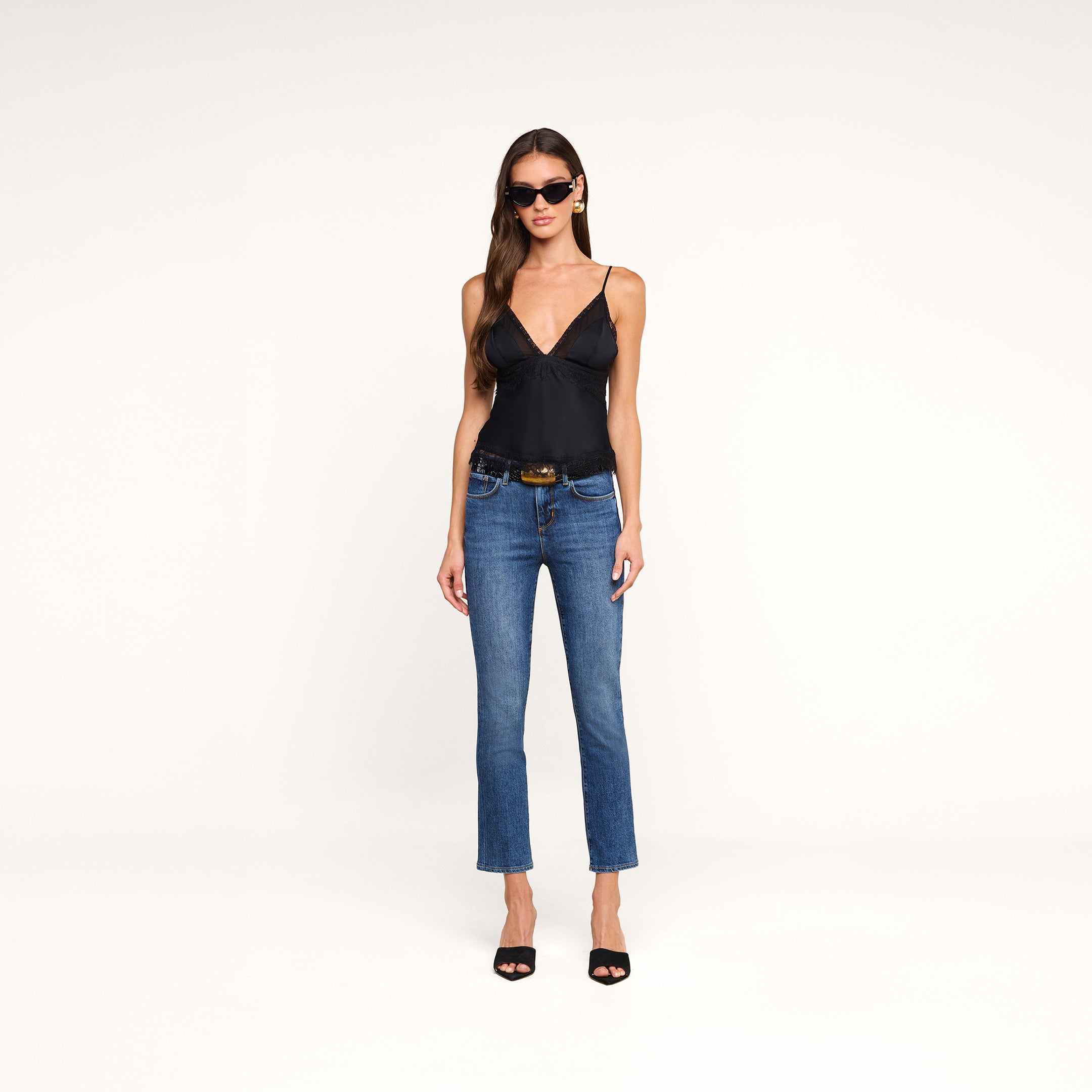 A woman wearing sunglasses, blue jeans, a black belt, black heels, and the Elka Satin Lace Camisole stands against a plain white background.