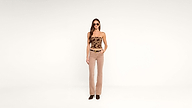 A woman wearing sunglasses, a strapless patterned top, beige pants, and black shoes stands against a plain white background with one hand in her pocket.