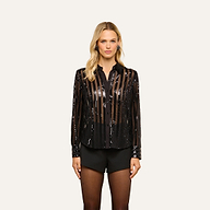 A woman is wearing the Dyana Sequin Blouse—a black, sheer striped long-sleeve sequin top—styled over a black bra and paired with black shorts and tights, standing against a plain light background.