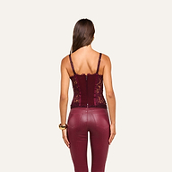 A woman stands with her back to the camera, wearing the Jenny Lace Bustier in burgundy and matching high-waisted leather pants, accessorized with a gold bracelet on her left wrist, set against a plain beige background.