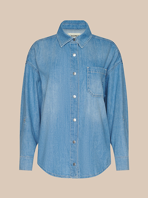 La chemise surdimensionnée Jorah est une chemise à boutons en denim bleu clair avec des manches longues, un col et une poche poitrine unique, sur un fond beige uni.