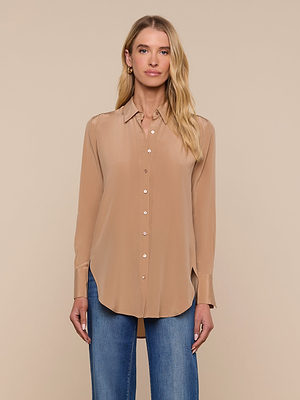 A woman with long blonde hair wears the Babette Silk Blouse—a tan, long-sleeve, relaxed-fit silk top—paired with blue jeans, standing against a plain beige background and facing forward with a neutral expression.