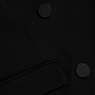 Close-up of the Rhoda Top in black fabric, showcasing two large round buttons and a partial belt or strap crossing diagonally at the lower section, stylishly paired with a suiting vest.