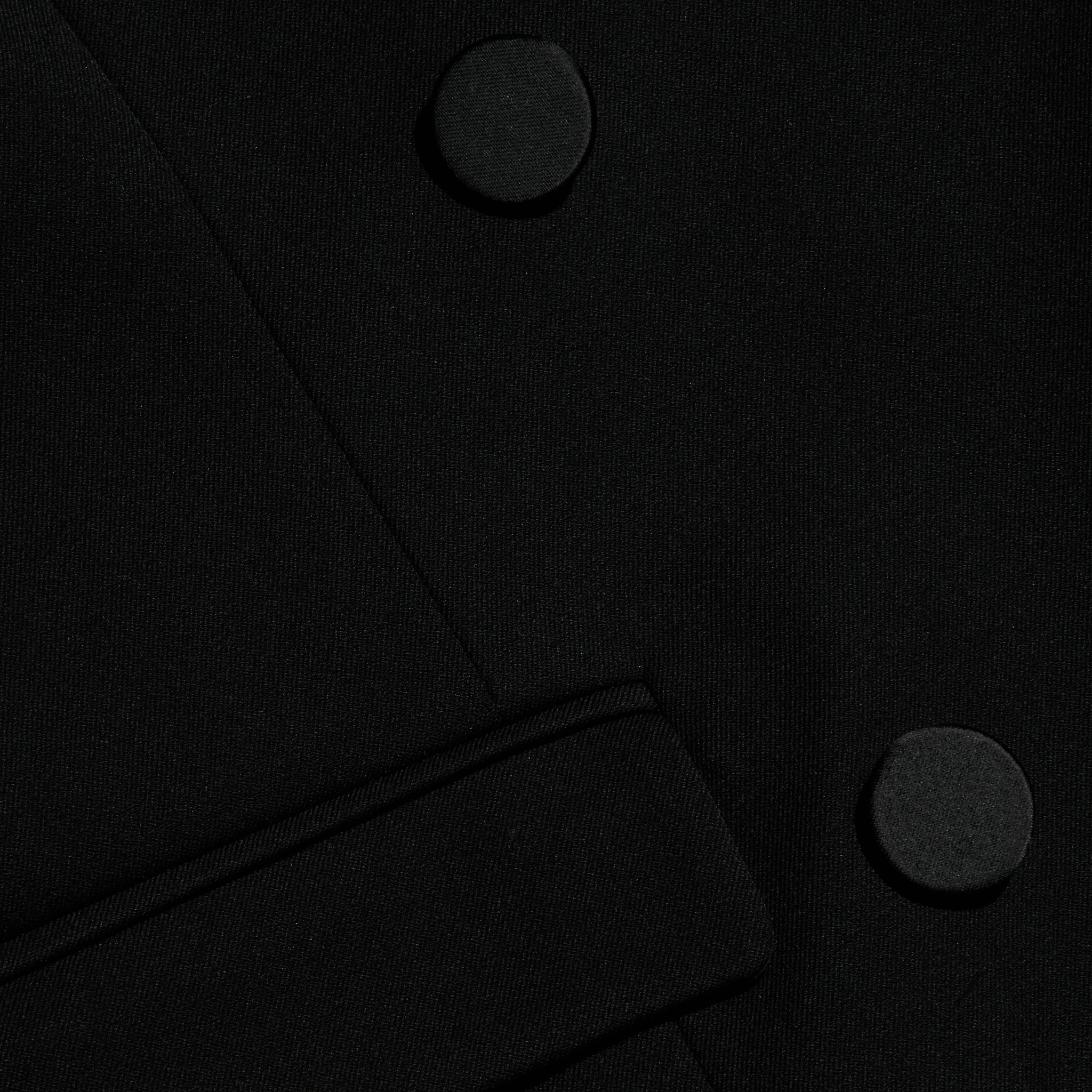 Close-up of the Rhoda Top in black fabric, showcasing two large round buttons and a partial belt or strap crossing diagonally at the lower section, stylishly paired with a suiting vest.