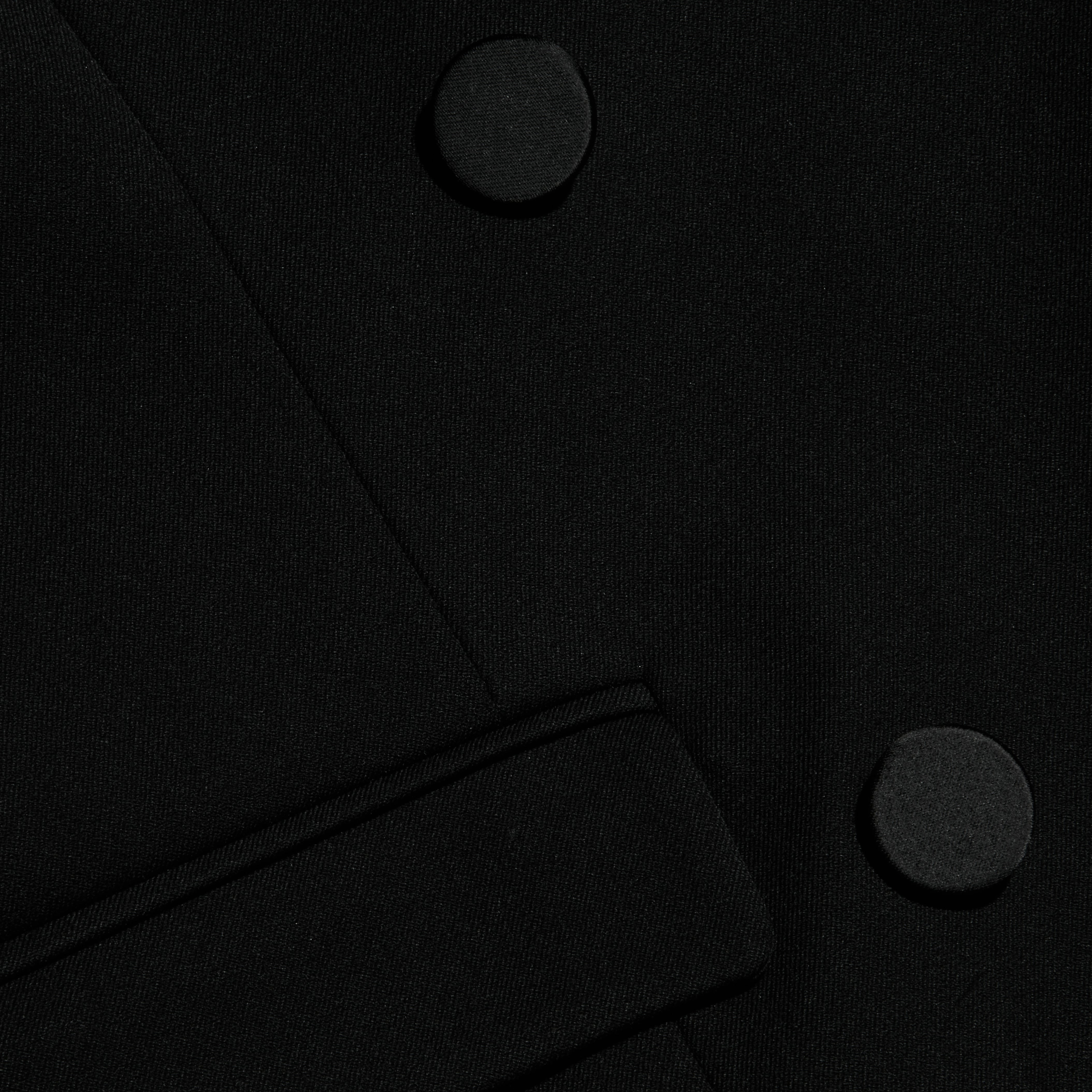 Close-up of the Rhoda Top in black fabric, showcasing two large round buttons and a partial belt or strap crossing diagonally at the lower section, stylishly paired with a suiting vest.