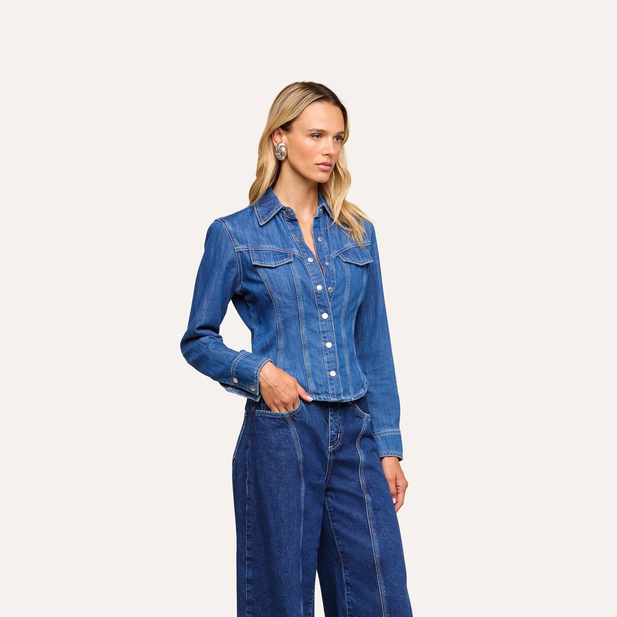 A woman wearing the Louis Fitted Shirt in featherweight denim and matching wide-leg jeans stands with one hand in her pocket against a plain light background.