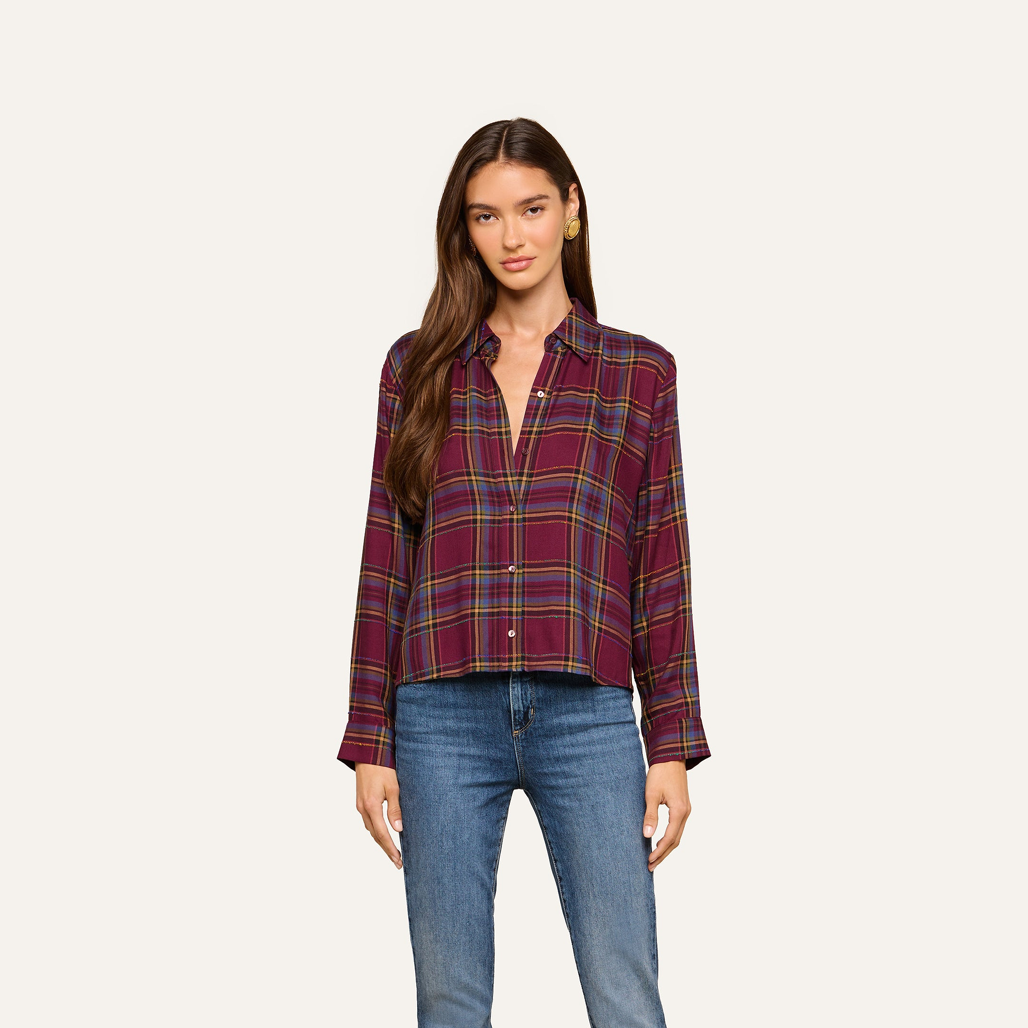 A woman with long brown hair wears the Suzette Shirt—a maroon plaid button-down—paired with blue jeans, standing against a plain light background.