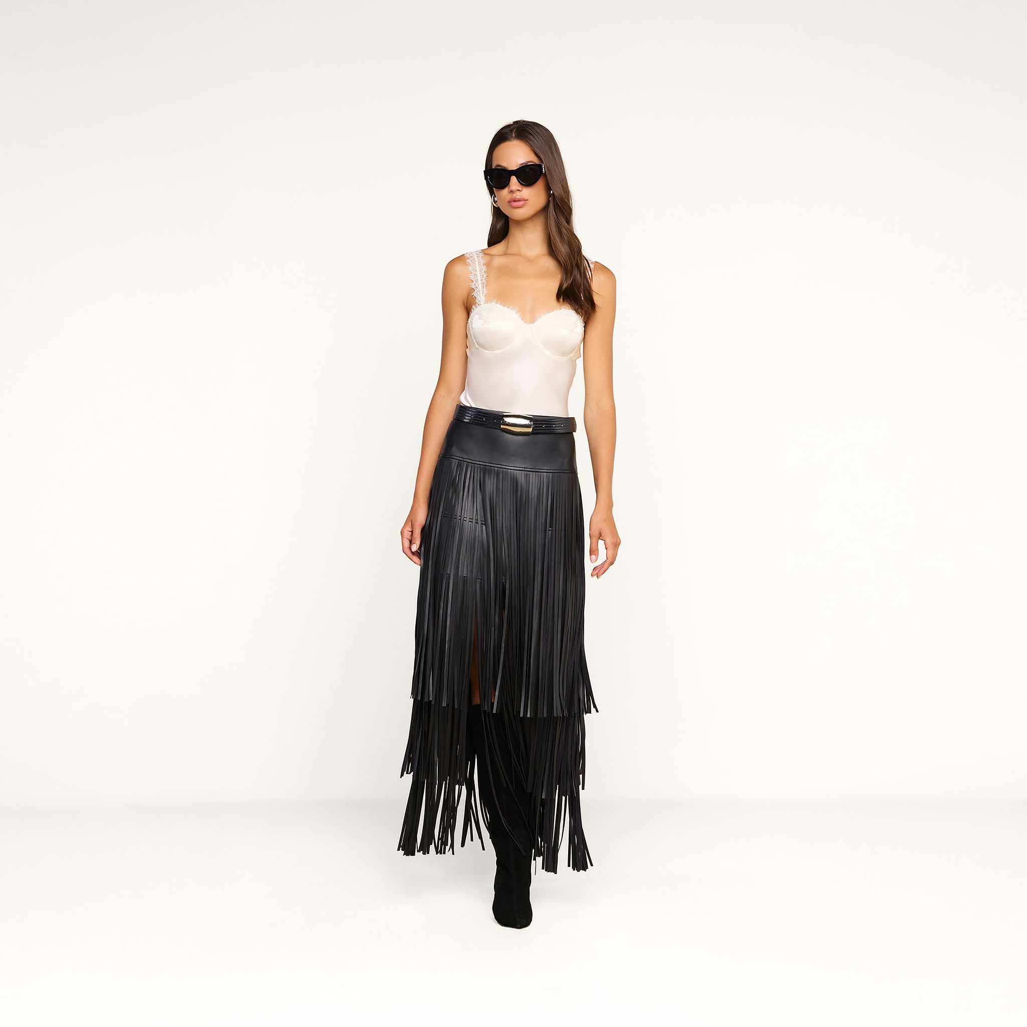 A woman wearing sunglasses, the Soleia Lace Camisole, and a black fringed skirt with boots stands against a plain white background.