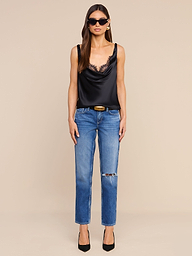 A woman wearing sunglasses, the Evadne Silk Lace Camisole, blue jeans with a rip on one knee, and black heels stands facing forward against a plain white background.