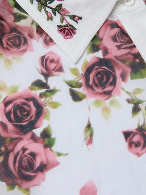 A close-up of the Philomena Blouse, a ramie button-down shirt with a collar embroidered with pink flowers and a main fabric printed with pink and red roses plus green leaves.