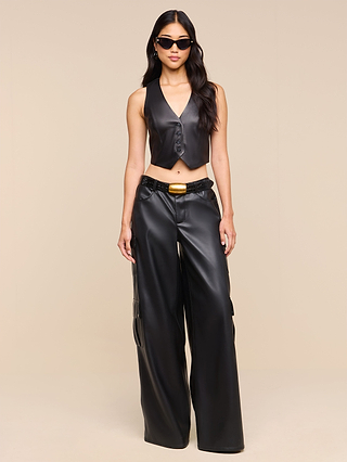 A person wearing sunglasses, the Jianna Leather Vest, and matching wide-leg leather pants stands against a beige background—an effortless nod to Fall 2026 fashion.