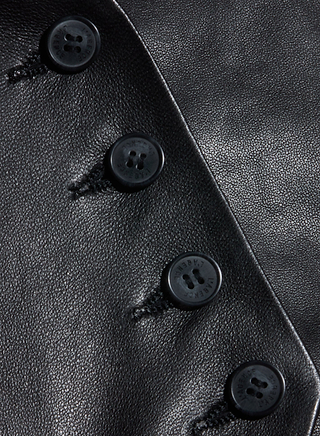 Close-up of four black buttons sewn onto shiny black leather, arranged diagonally—a sleek detail from the Jianna Leather Vest, a must-have cropped piece for Fall 2026.