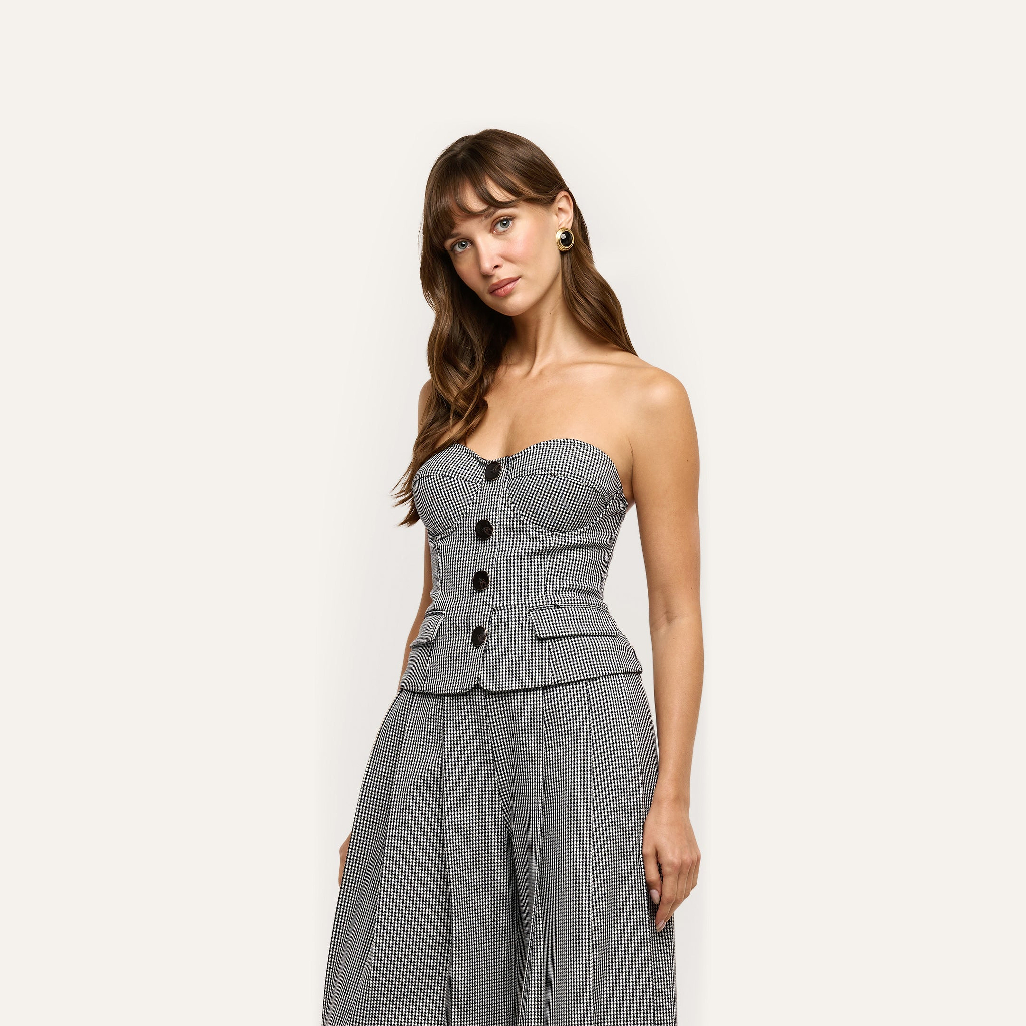 A person wearing the Genevieve Corset Top, a strapless, black and white houndstooth suiting corset with a buttoned front and a peplum hem.