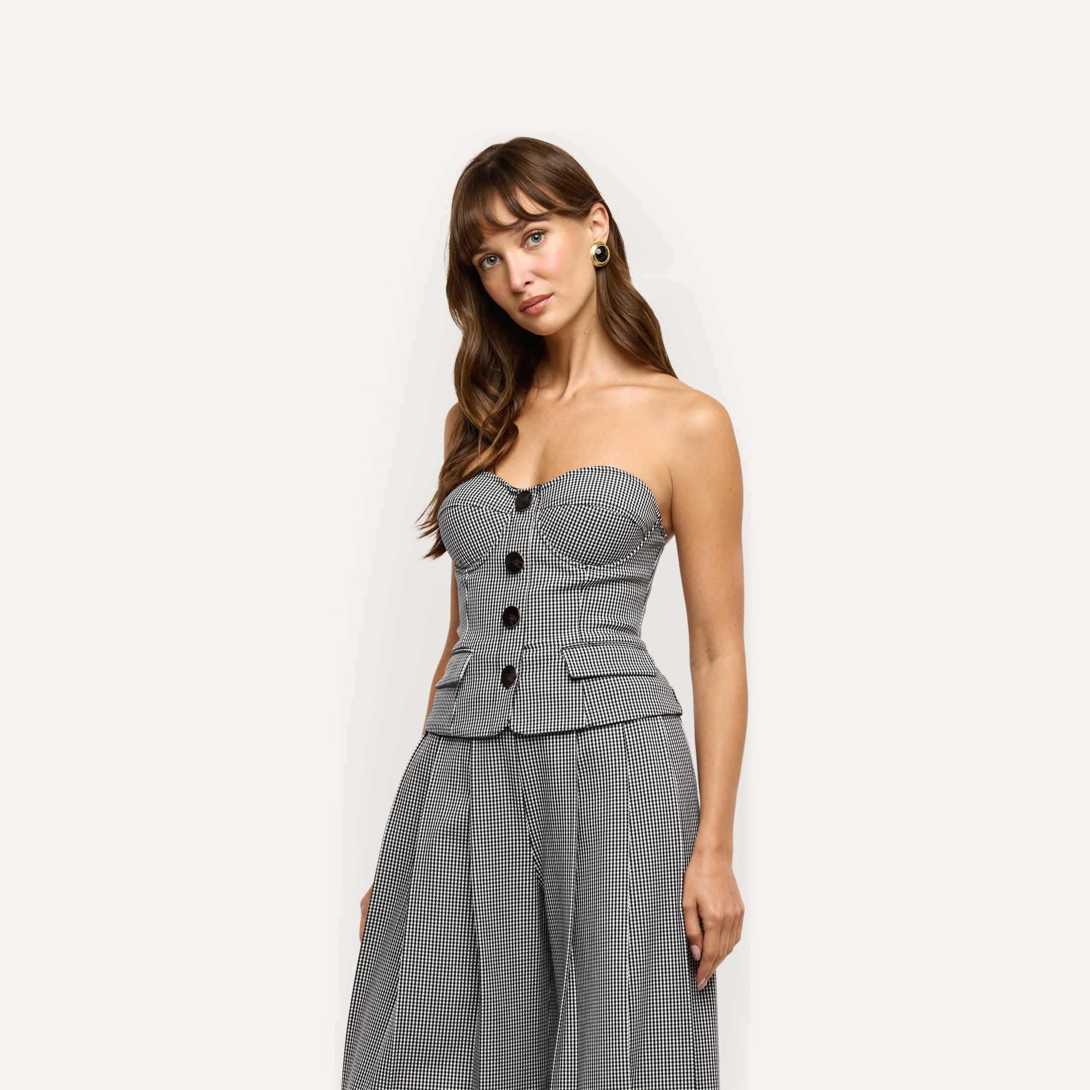 A person wearing the Genevieve Corset Top, a strapless, black and white houndstooth suiting corset with a buttoned front and a peplum hem.