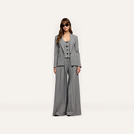 A woman wearing a black and white Genevieve Corset Top, matching houndstooth suiting blazer, and wide-leg trousers, styled with dark sunglasses.
