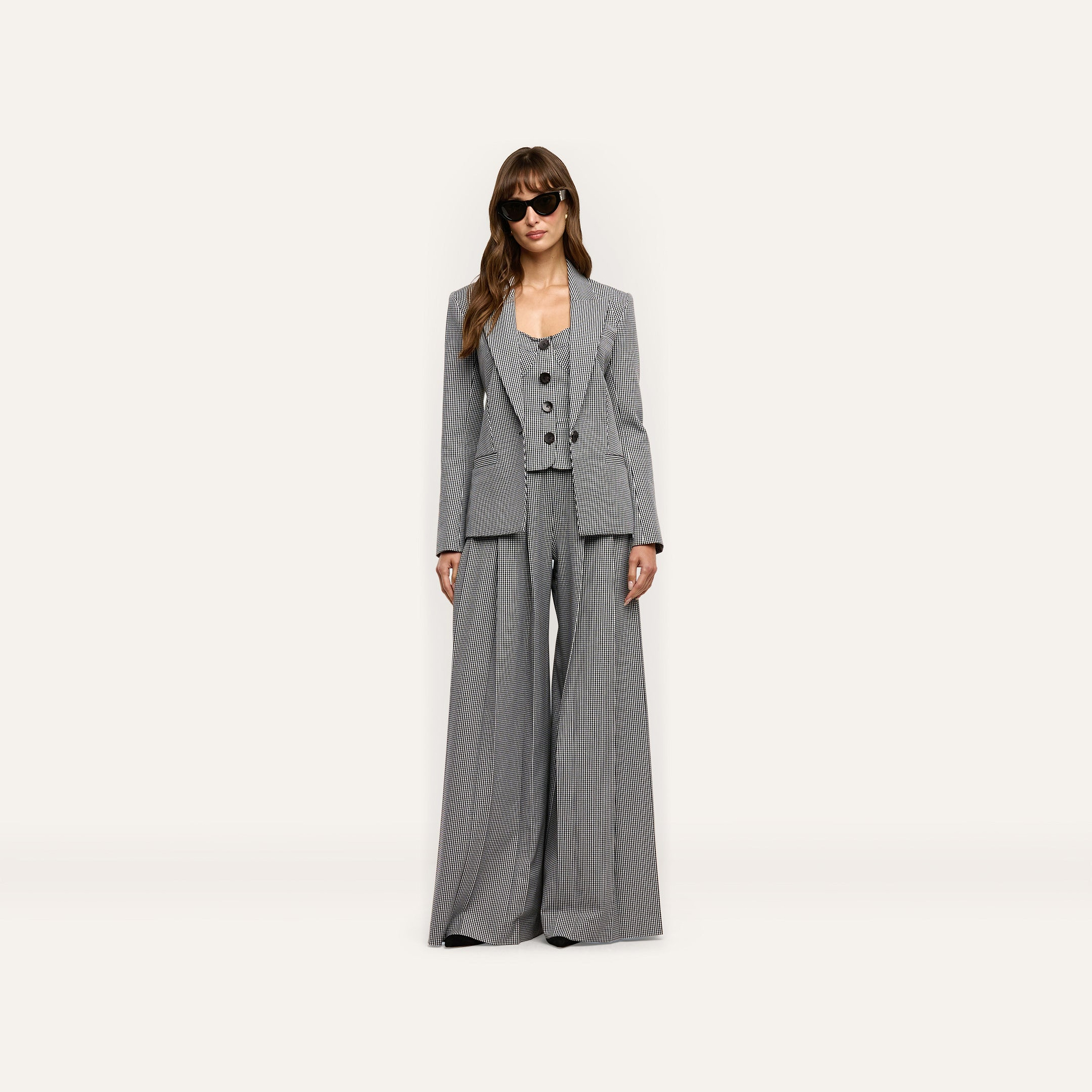 A woman wearing a black and white Genevieve Corset Top, matching houndstooth suiting blazer, and wide-leg trousers, styled with dark sunglasses.
