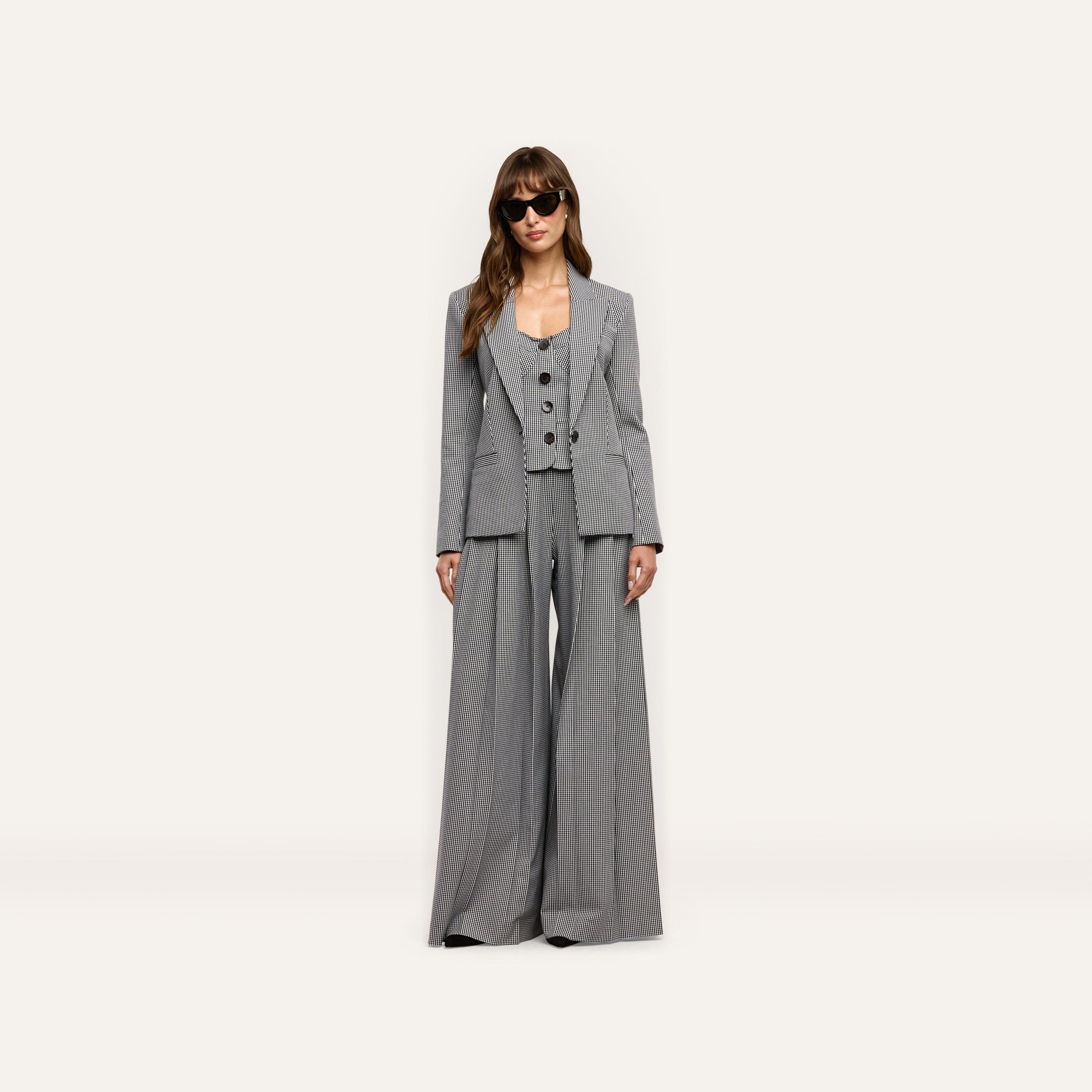 A woman wearing a black and white Genevieve Corset Top, matching houndstooth suiting blazer, and wide-leg trousers, styled with dark sunglasses.