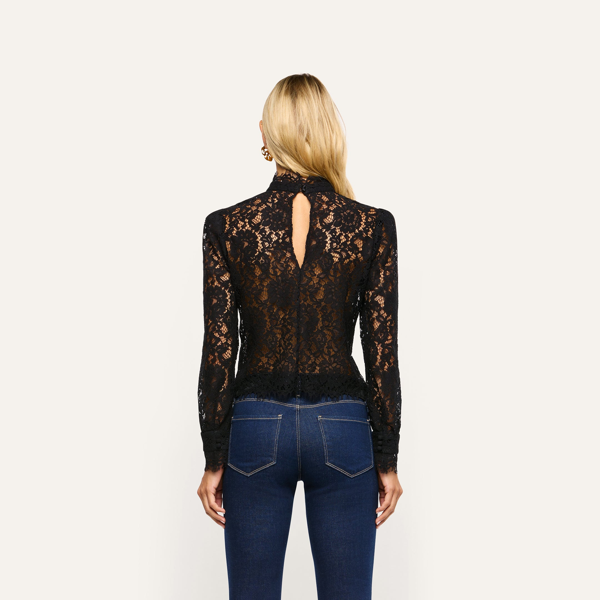 Back view of an Amarenthe Lace Blouse, a long-sleeved corded lace mockneck top featuring a teardrop cutout, worn with blue jeans.