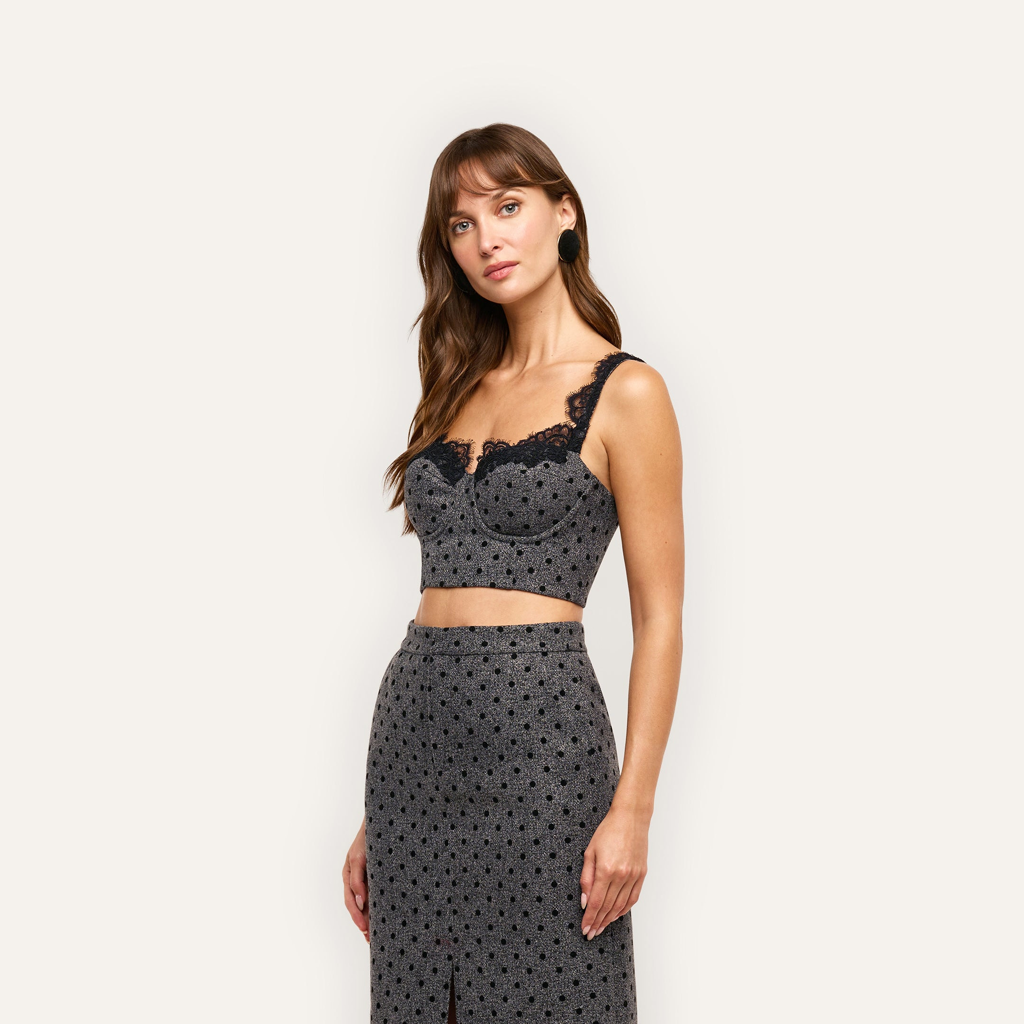 A woman wears an Oriane Bustier Top, a grey, polka-dot cropped bustier with built-in underwire and black lace trim along the neckline.