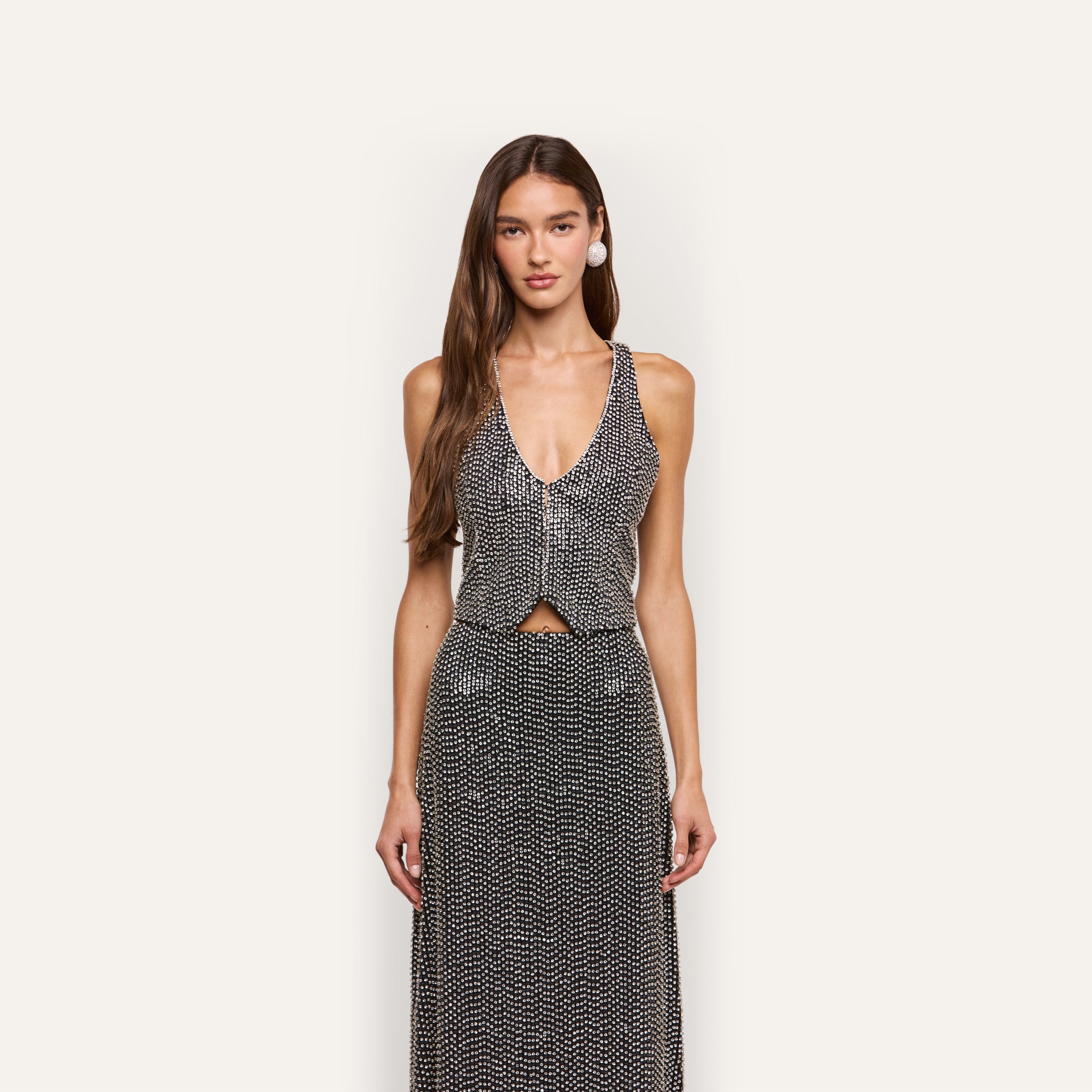 A woman wearing a black, hand-embellished Nixe Embellished Vest with sequins and crystals paired with a matching maxi skirt.