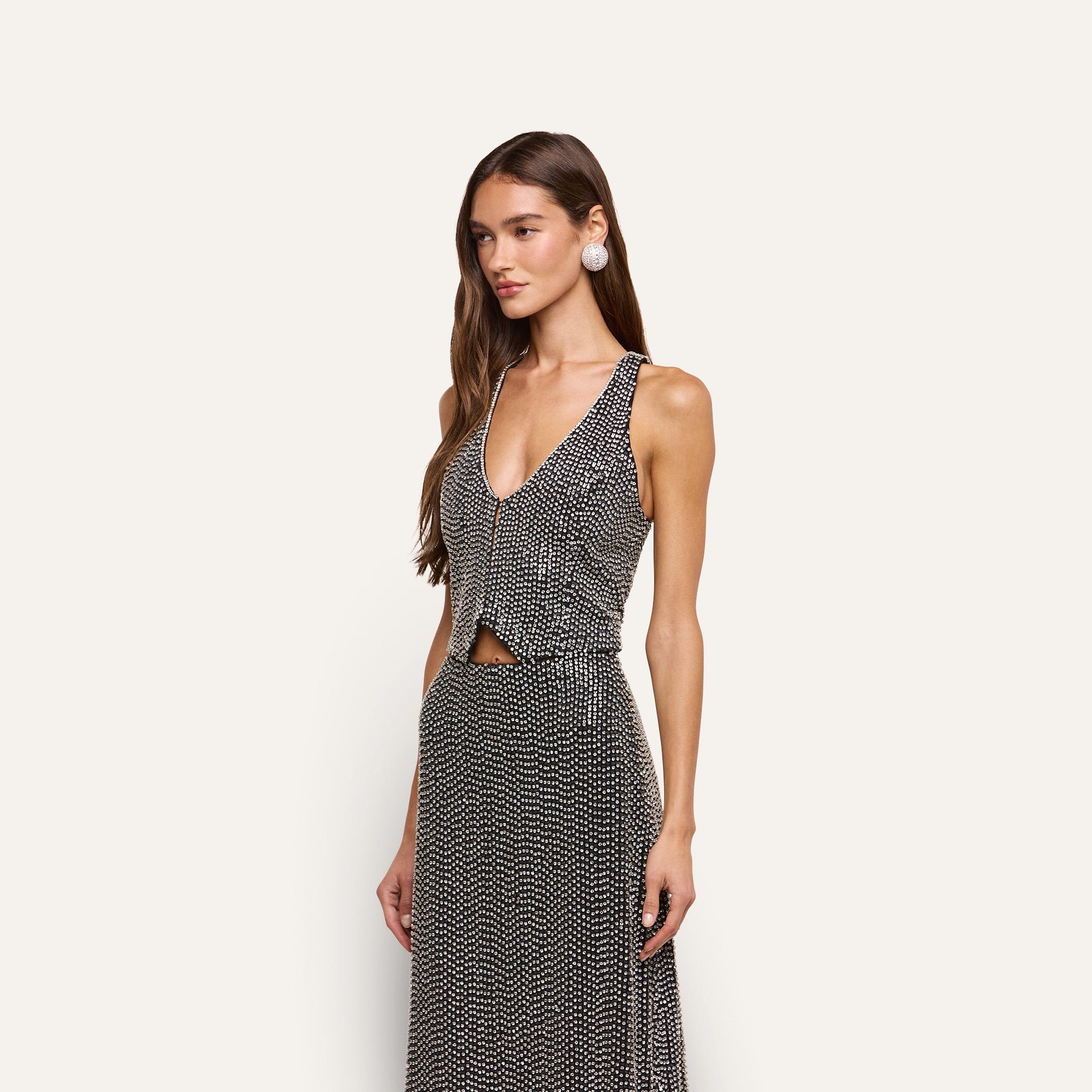 A woman wears the Nixe Embellished Vest, a sleeveless, deep-V neck cropped vest hand-embellished with silver sequins and crystals.