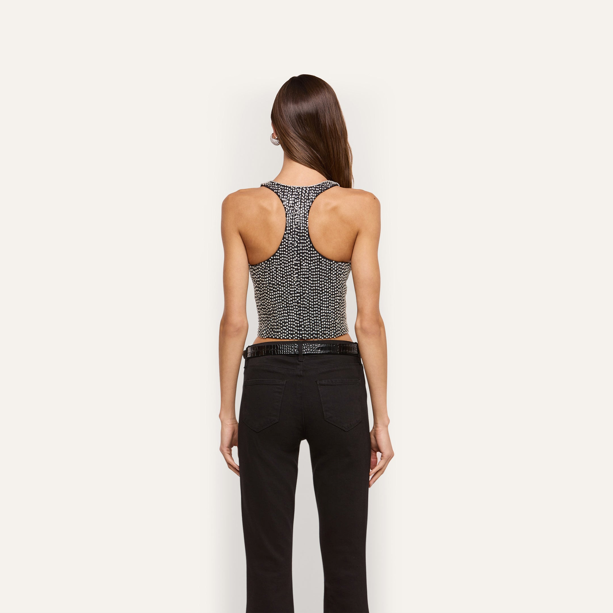 A person seen from behind wearing the Nixe Embellished Vest, a cropped, hand-embellished racerback style covered in small crystals, paired with black pants.