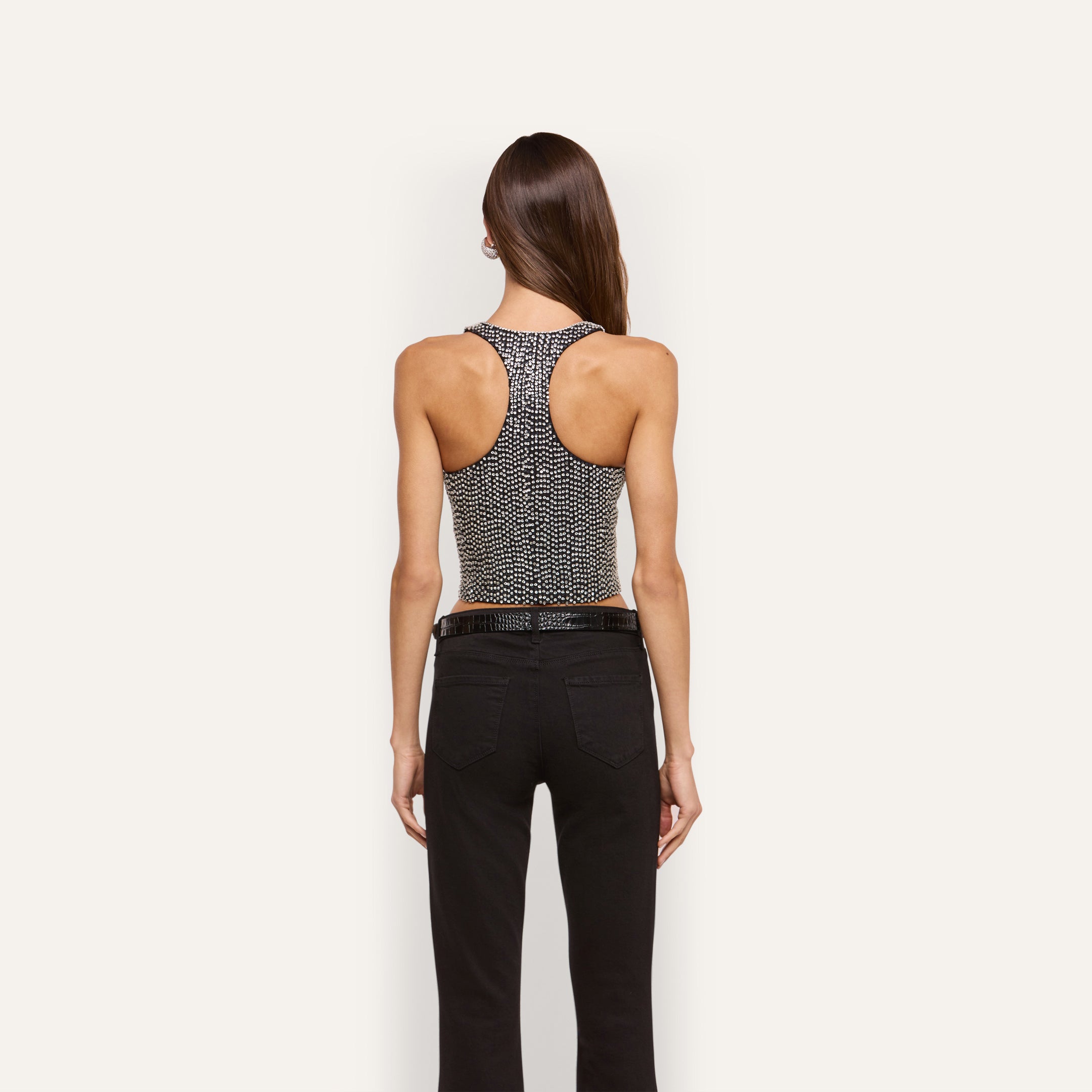 A person seen from behind wearing the Nixe Embellished Vest, a cropped, hand-embellished racerback style covered in small crystals, paired with black pants.
