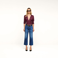 Woman in sunglasses wearing the Nina Silk Blouse—a relaxed fit, red patterned top—styled with blue cropped jeans, a black belt, and black high heels stands against a plain white background.