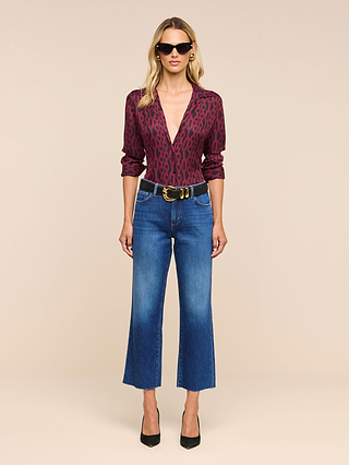 Woman in sunglasses wearing the Nina Silk Blouse—a deep red patterned button down—paired with blue cropped jeans with frayed hems, a black belt, and black heels, standing against a beige background.